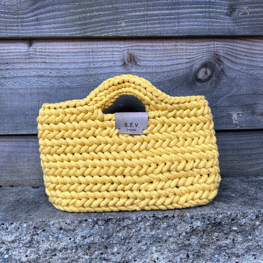 Gele gehaakte Syl tas 'Yellow' van S.E.V. Originals op een stenen rand, te koop bij De Garengarage.